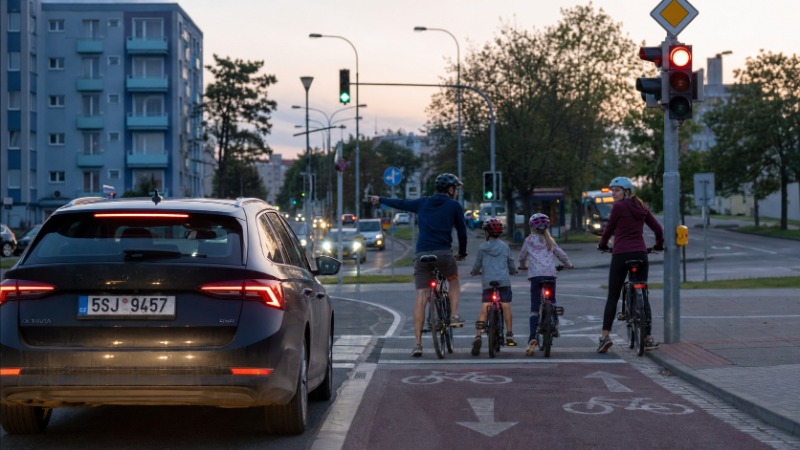 Cyklista s přilbou a rozsvíceným zadním světlem jede po kraji silnice za soumraku