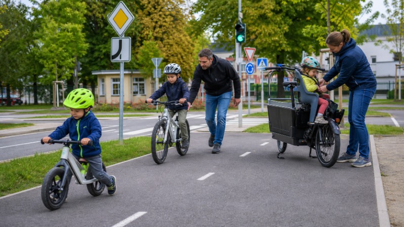 Rodič s dítětem v cyklistické přilbě jedou vedle sebe po cyklostezce
