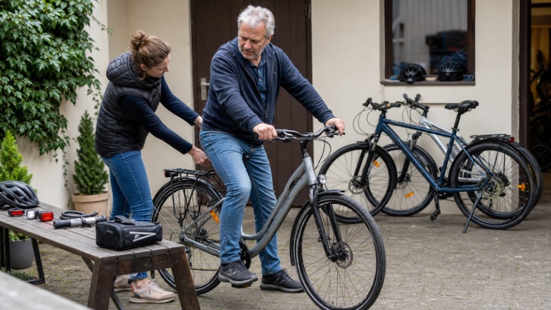 Dospělý cyklista v helmě stojí s novým trekovým kolem na cyklostezce